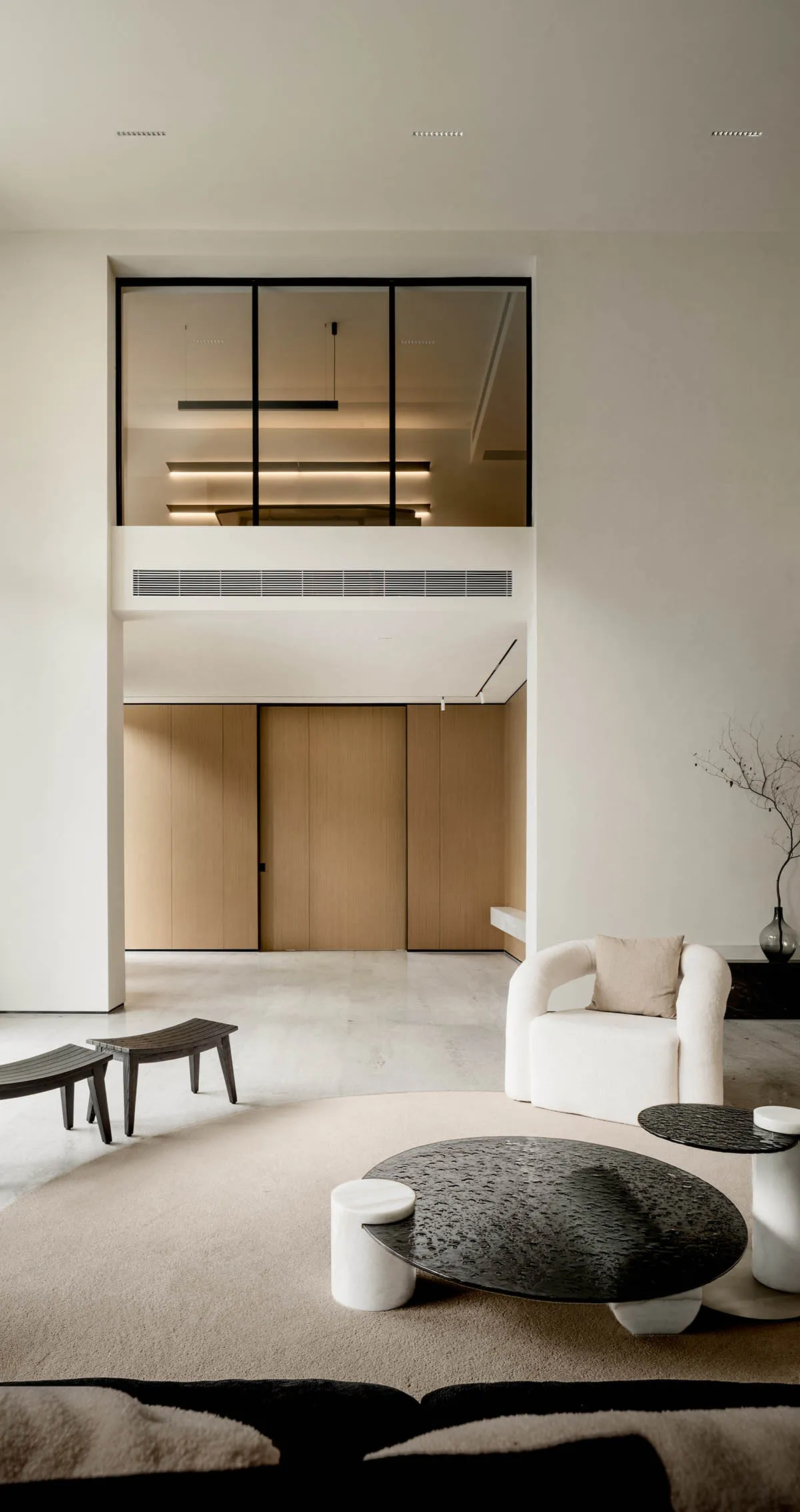 A minimalist living room with concrete finishes, featuring a white armchair, black coffee table, and wooden panels on the wal