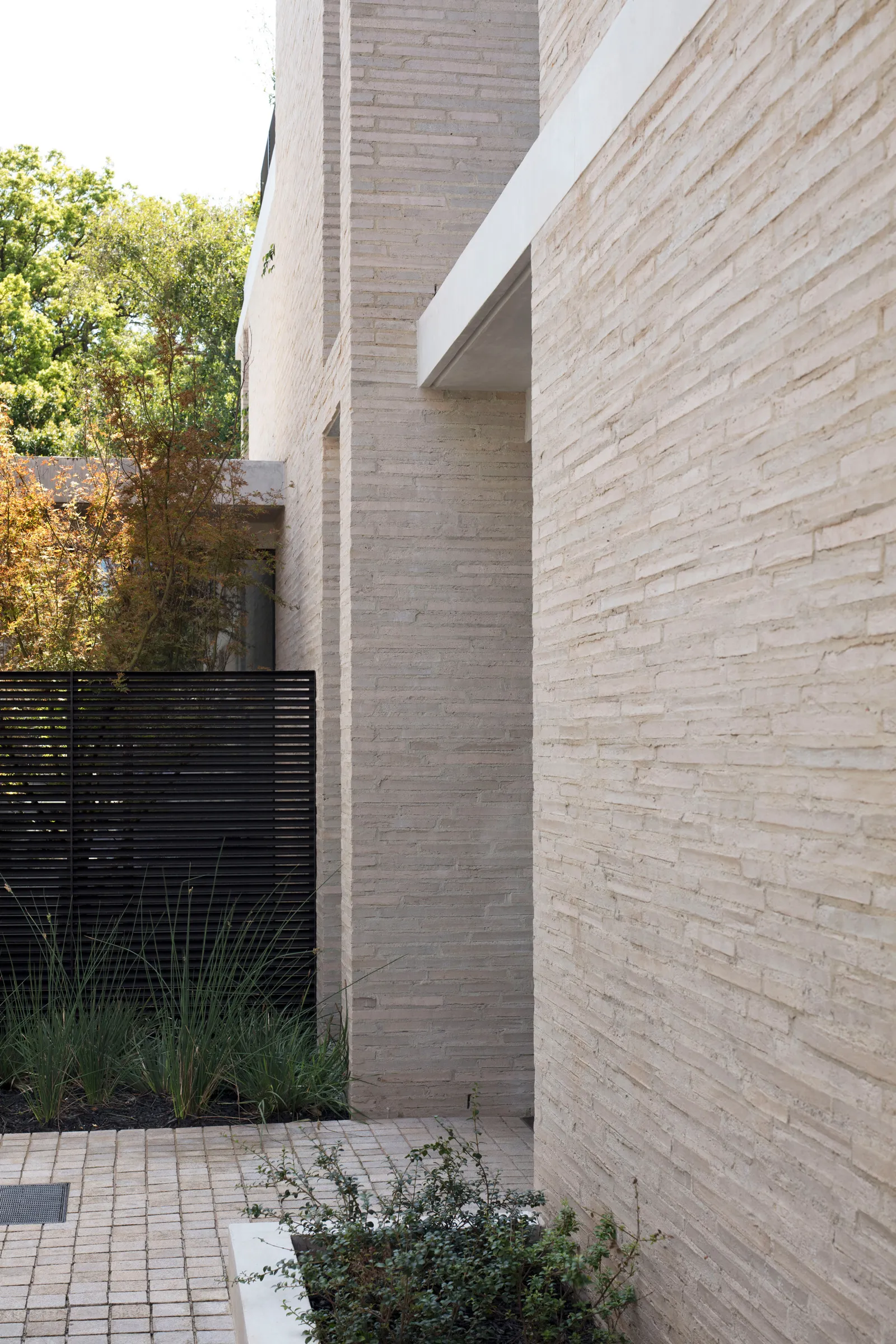 A minimalist building exterior with concrete walls and a black fence in front of tall trees.