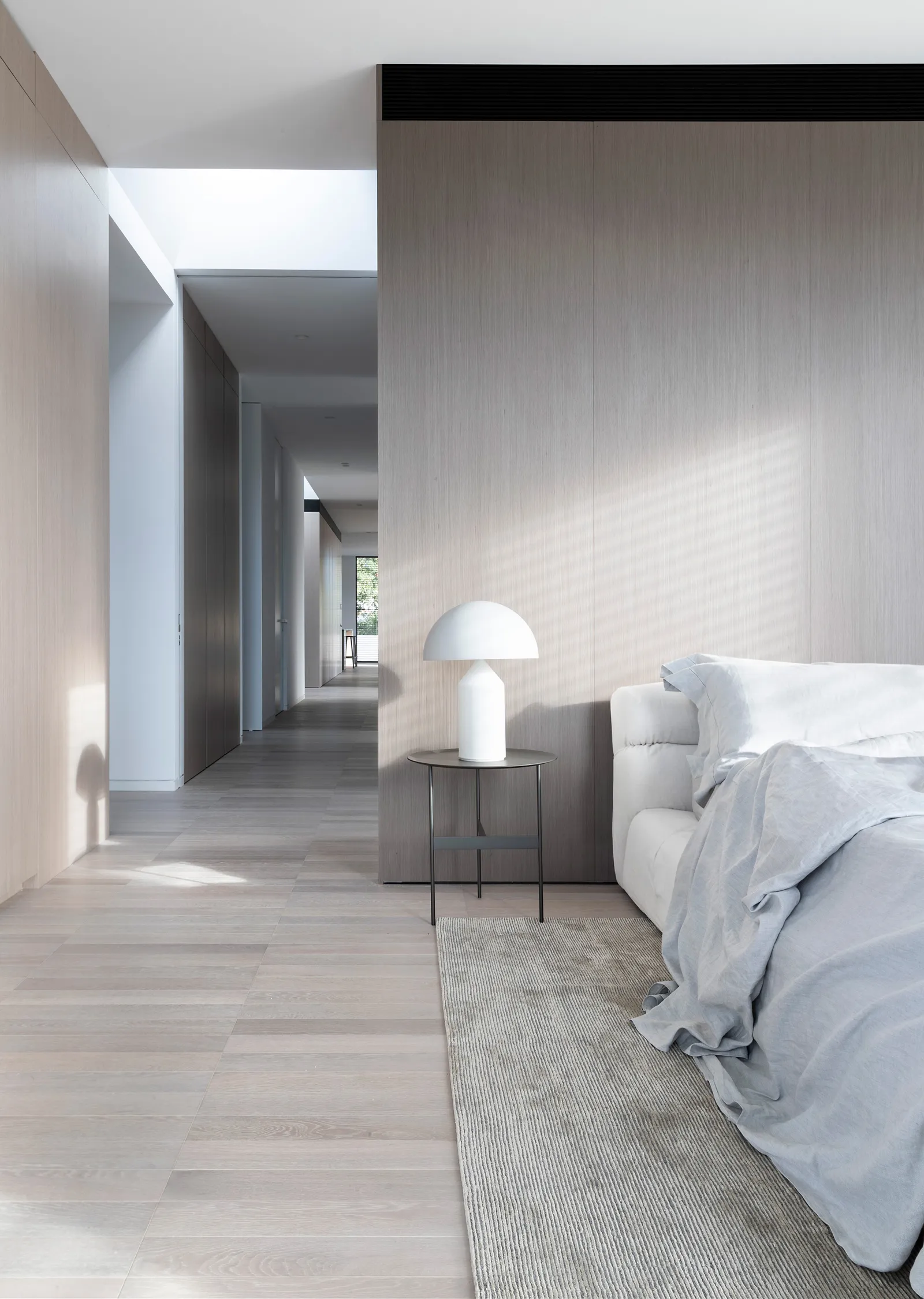 A modern bedroom featuring wooden paneling, a white lamp, and a comfortable-looking bed.