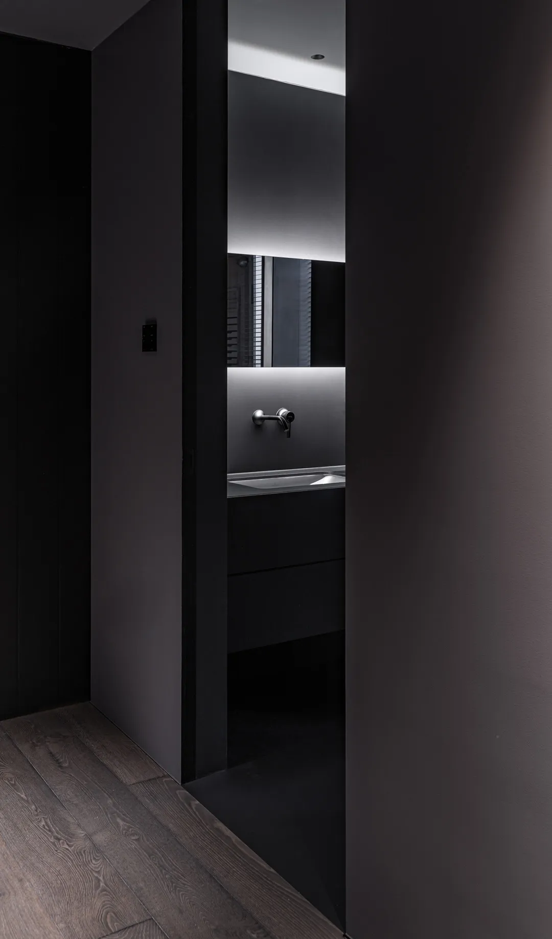 A modern black bathroom with an illuminated mirror and metallic fixtures.