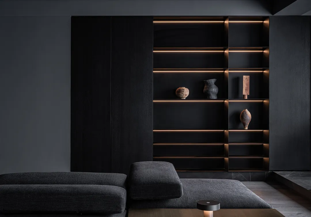 A modern minimalist black shelf with wood elements displaying decorative ceramic objects.