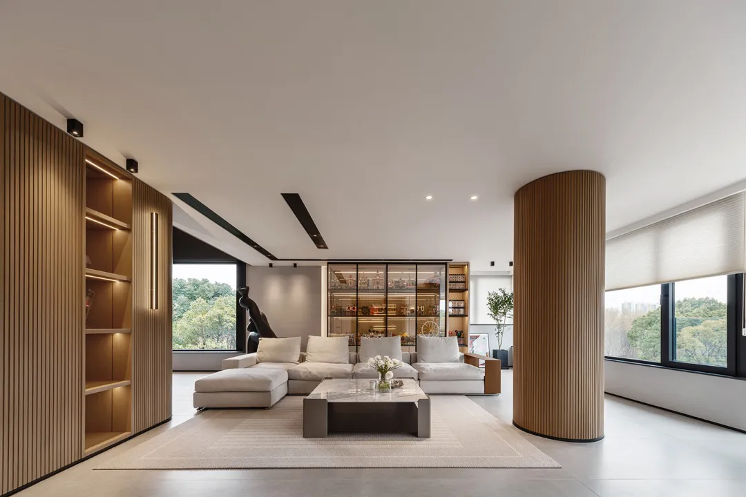 A modern living room with wooden columns, a white rug, and a large window overlooking greenery.