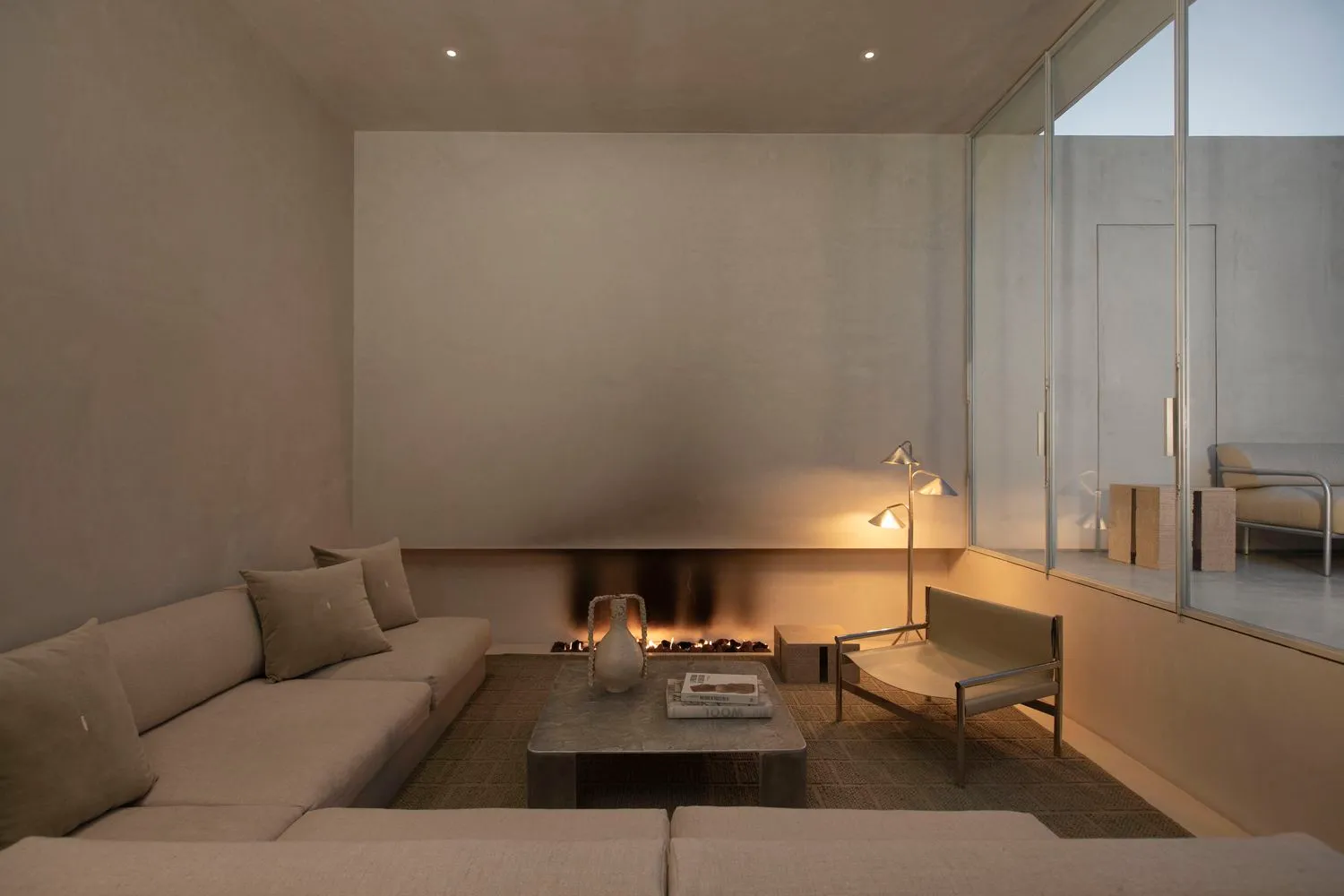 A minimalist living room featuring concrete walls and flooring with a cozy fireplace and comfortable seating.
