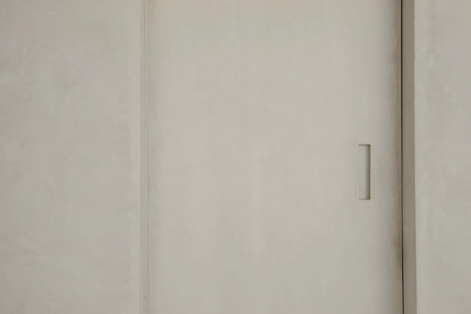 A minimalist interior featuring a grey concrete wall with a horizontal rectangular opening.
