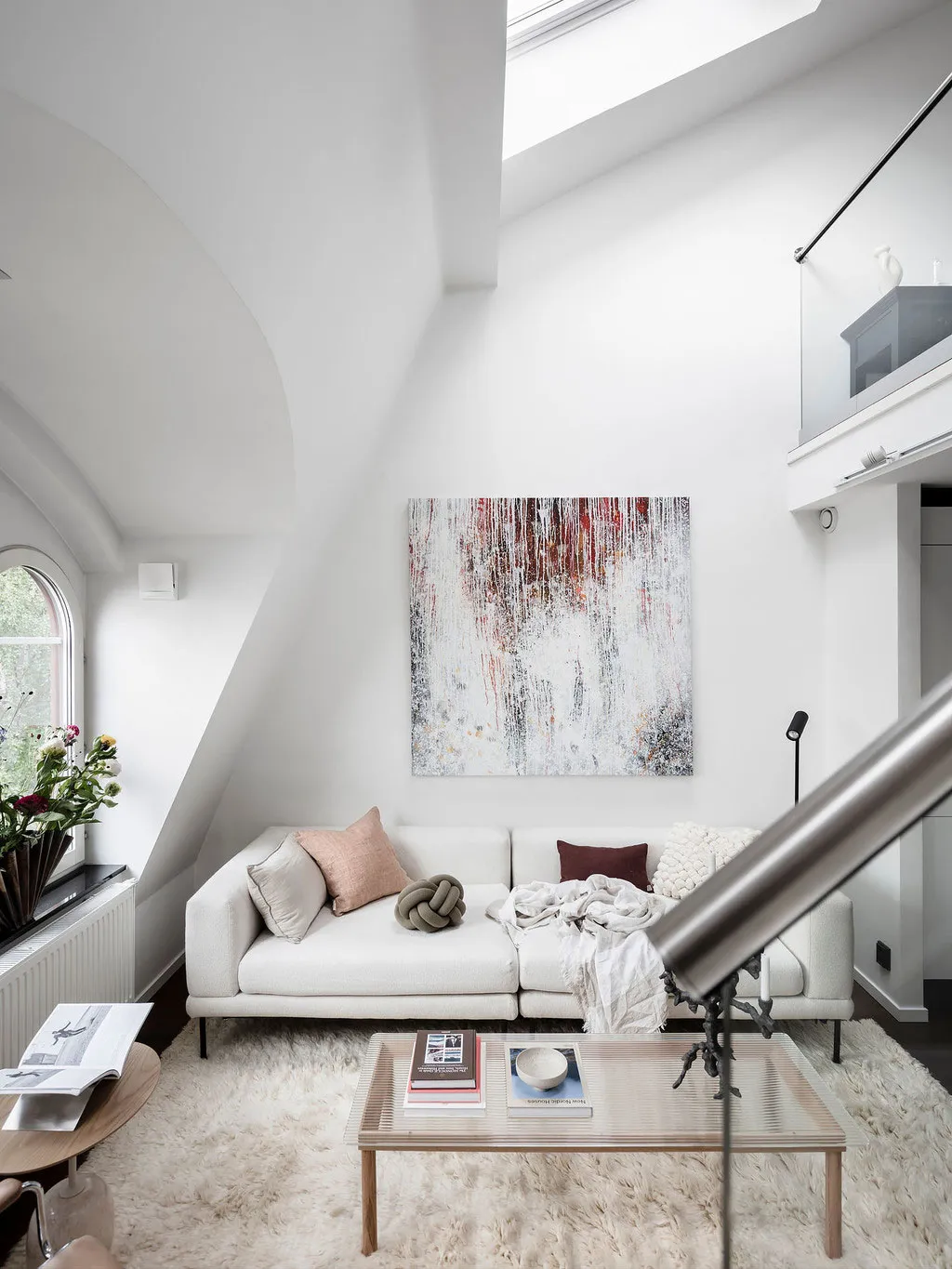 A modern living room with a white sofa, abstract art piece, and minimalist decor.