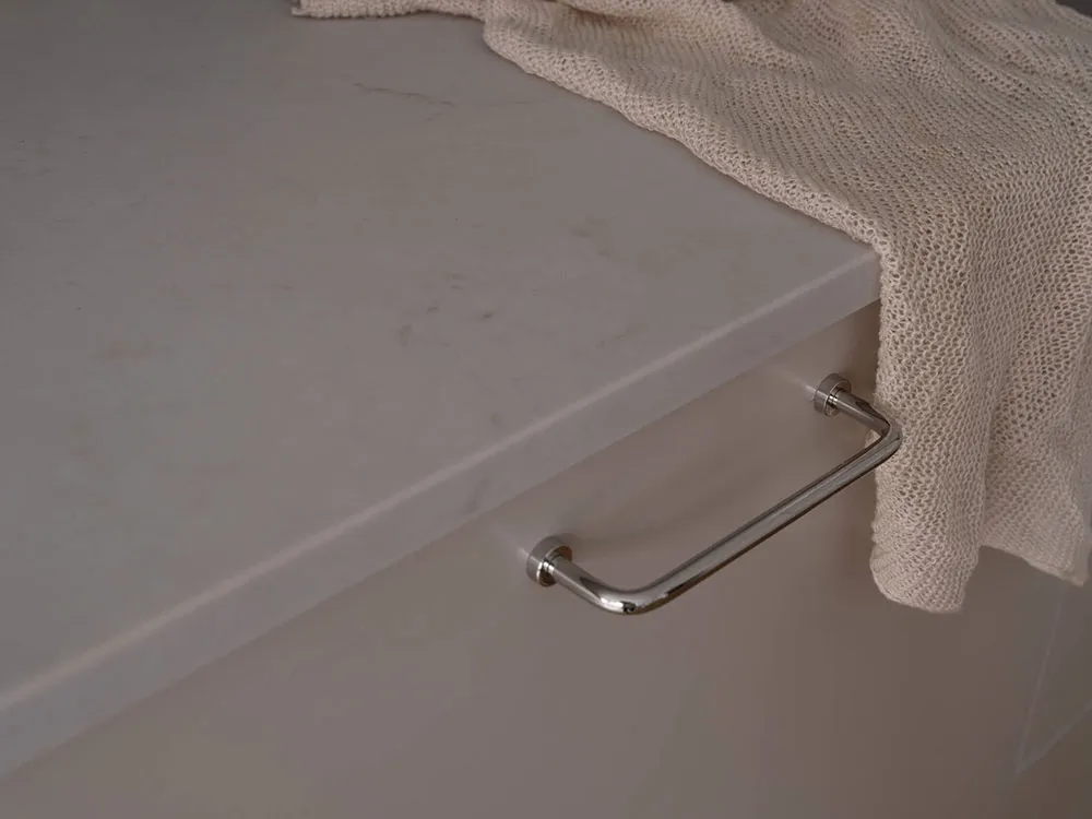 Close-up of a shiny chrome kitchen handle on a marble countertop, with a beige knitted towel draped over the edge.