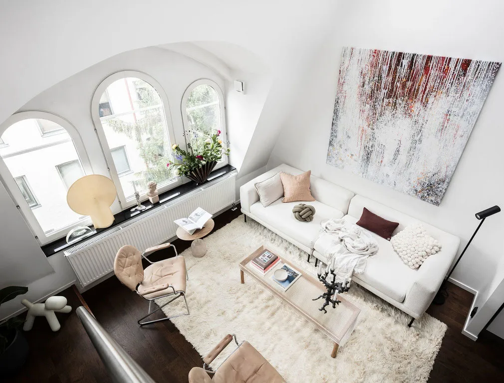 Modern, white-themed living room featuring a cozy sofa, minimalist chairs, and abstract art, designed for comfort and style.