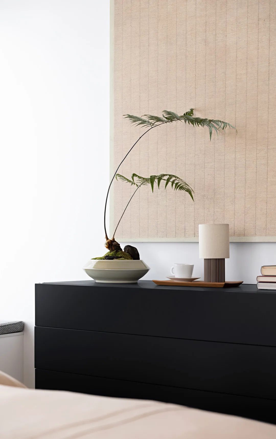 Minimalist bedroom featuring a black sideboard with a plant, a cup, and a lamp.