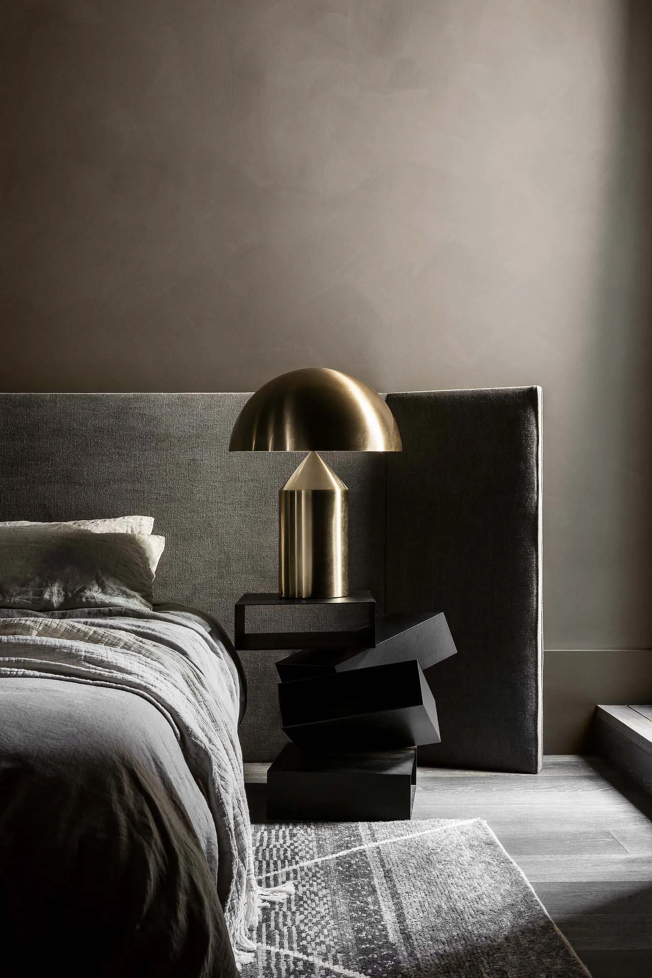 A minimalist bedroom with a metal side table, grey bedding, and a grey headboard.