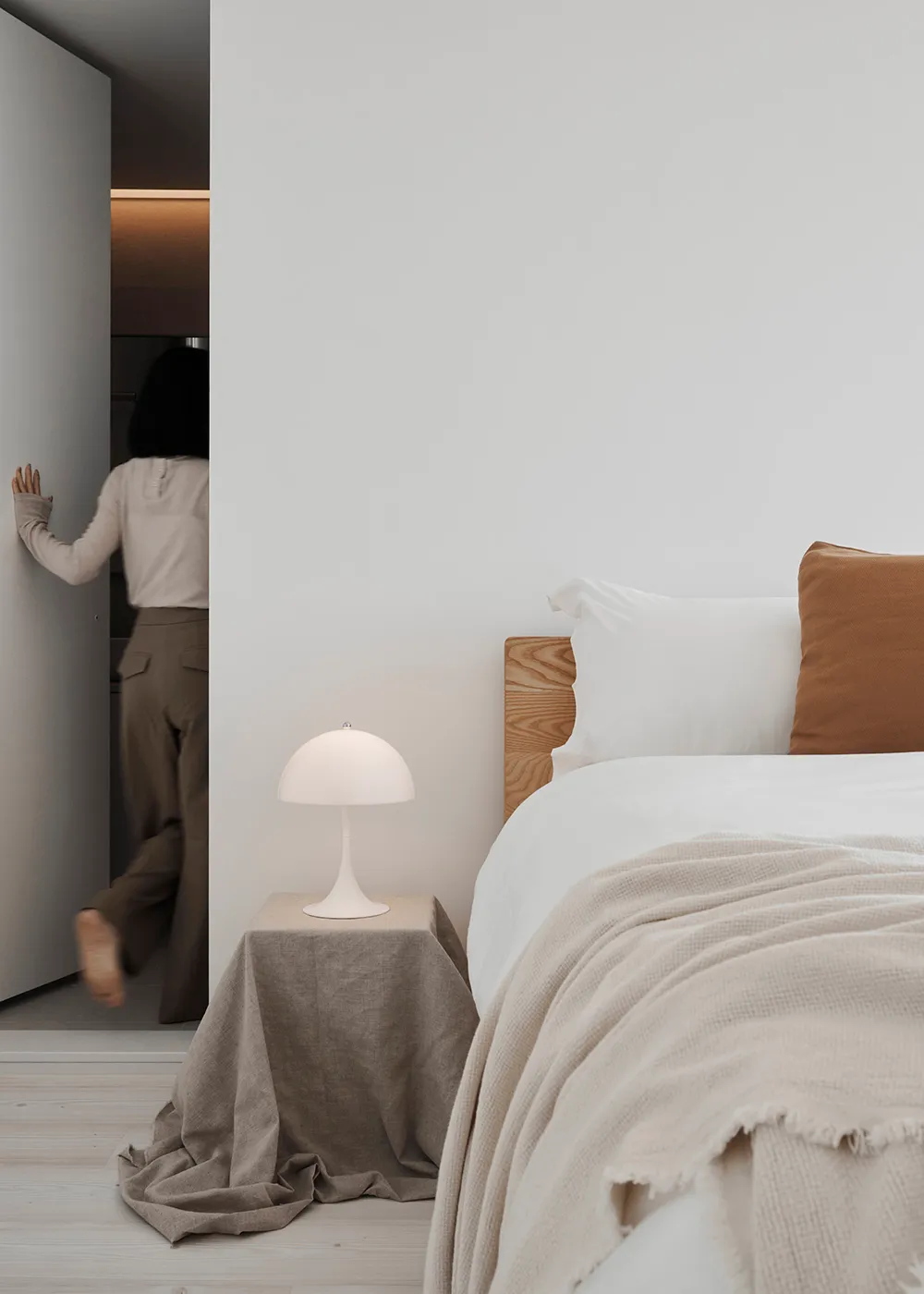A minimalist bedroom with a white wall, wooden bed frame, and beige bedding.