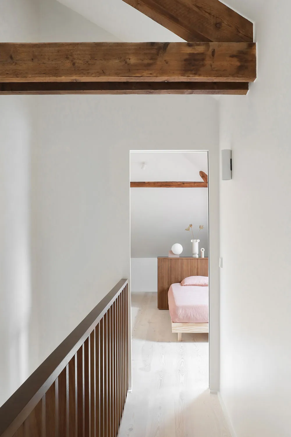 A minimalist bedroom with wooden beams on the ceiling and white walls.