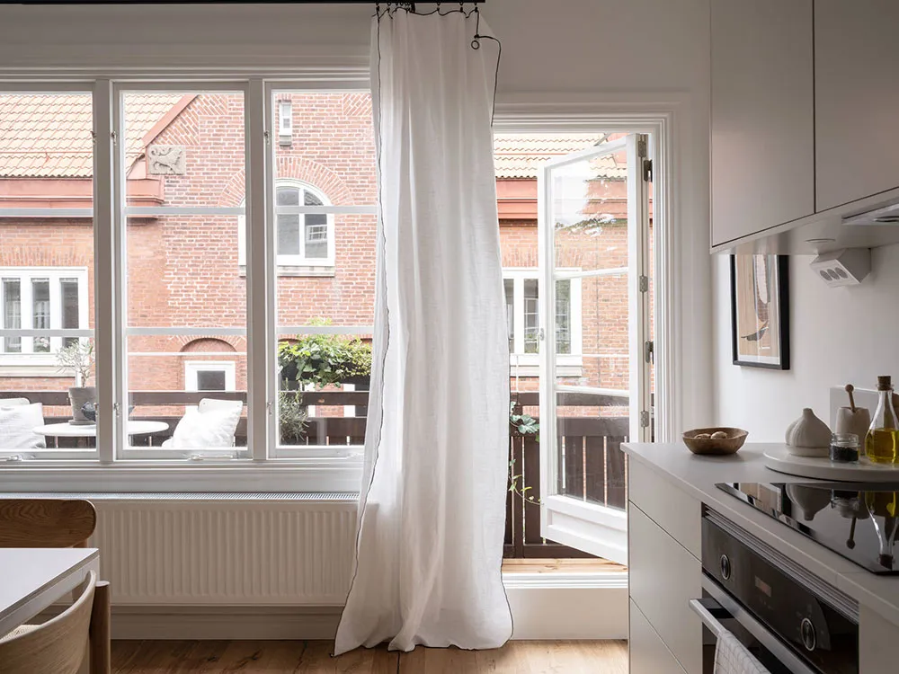 A minimalist residential kitchen with white walls, wooden cabinets, and glass windows.