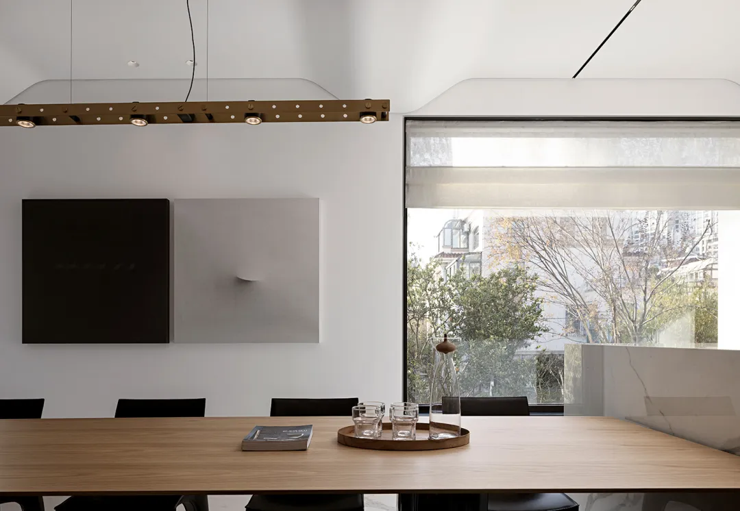Modern conference room with a wooden table, black chairs, and minimalist decor. Large window with city view.