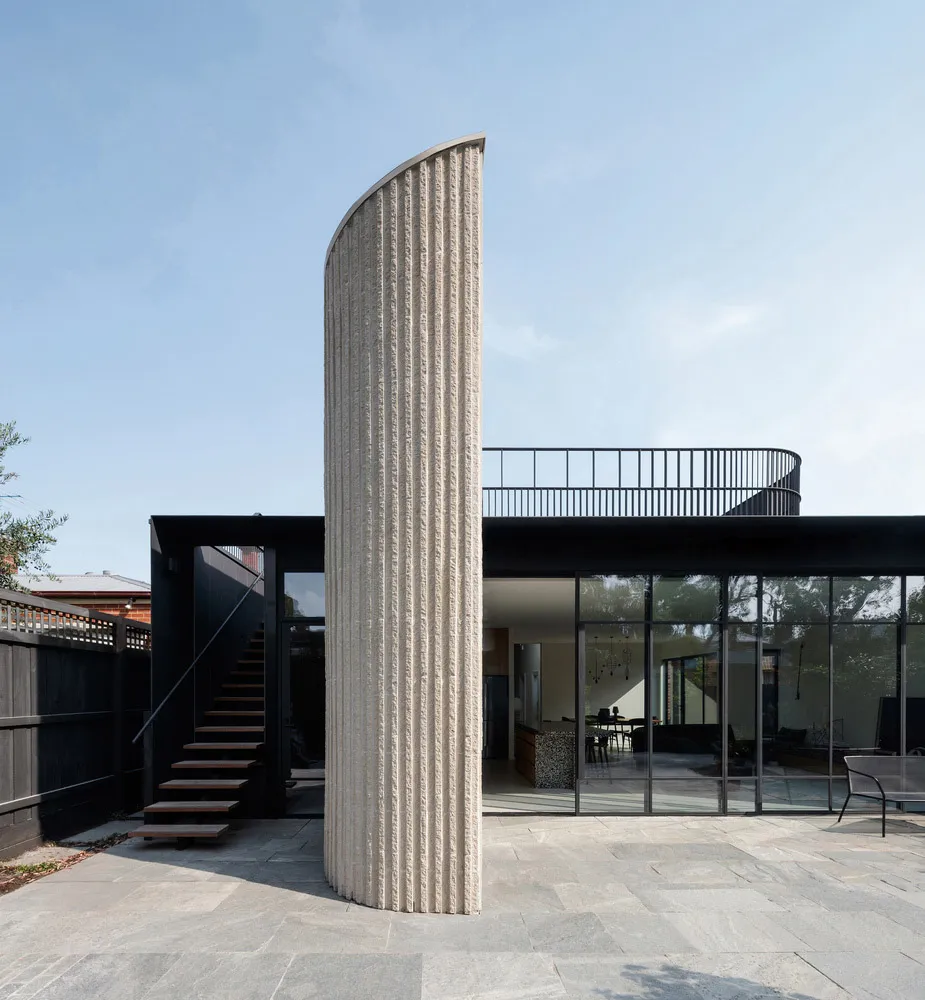 Modern exterior of a house with a curved concrete pillar, large glass windows, and black railings.