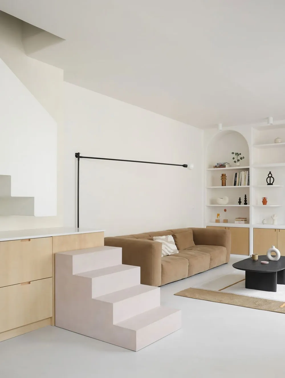 Minimalist living room featuring concrete steps leading to a seating area with a brown sofa and black coffee table, surrounde