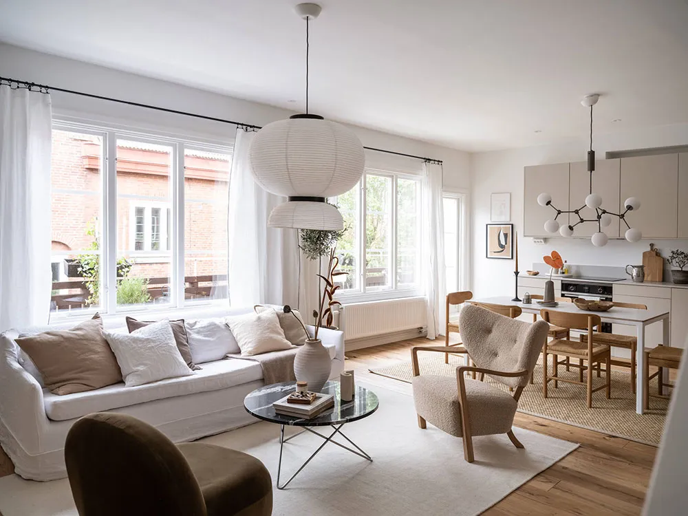 A modern, neutral-toned living room with a comfortable sofa, armchairs, and a dining area in the background.