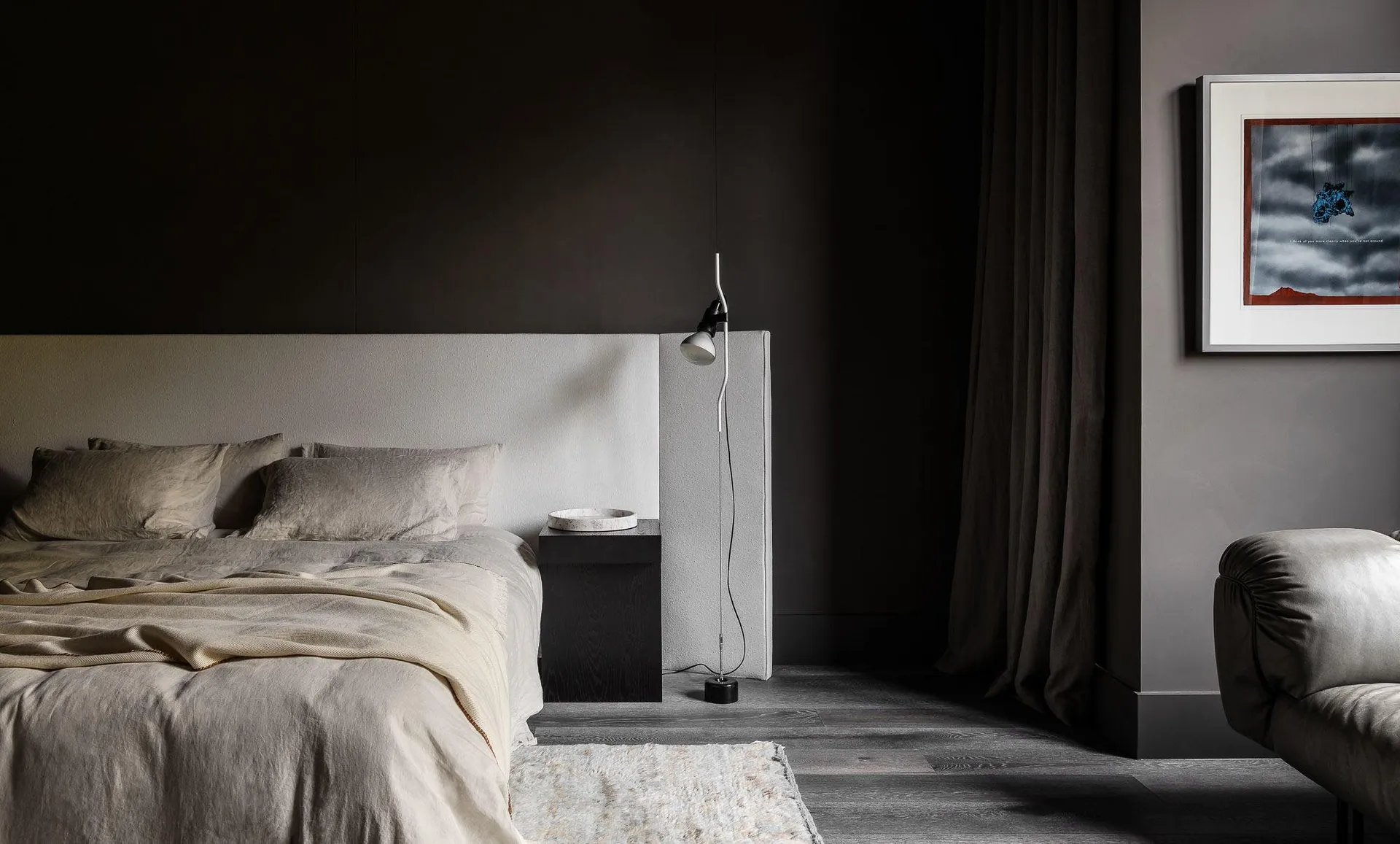 A minimalist bedroom with neutral textiles and a concrete bed frame, featuring blinds and a floor lamp.