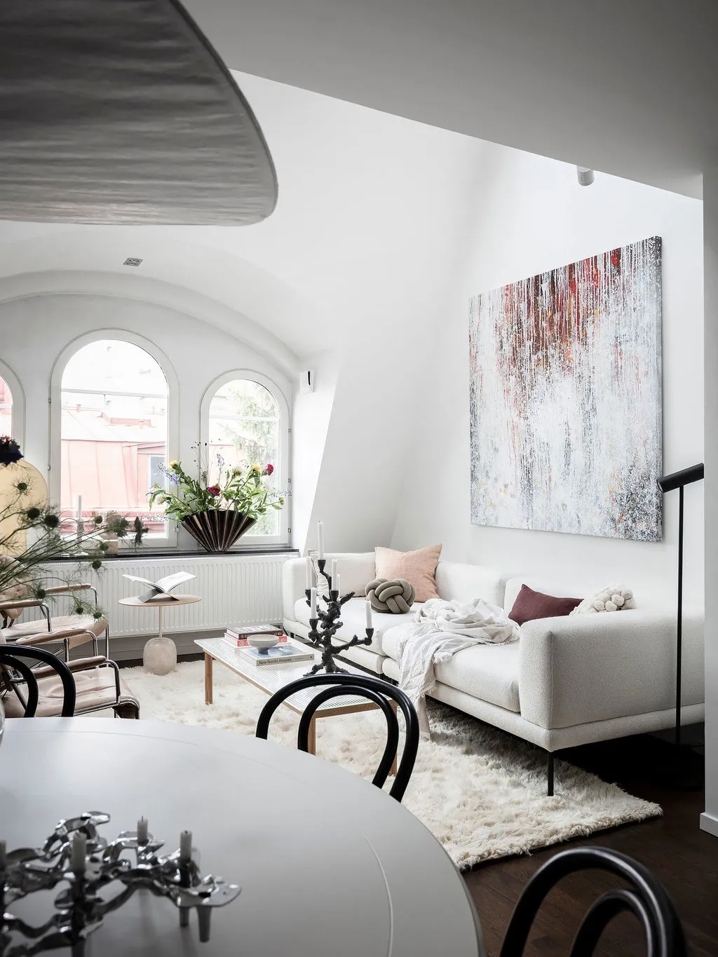 A modern, minimalist living room with a large white sofa, arched windows, and an abstract painting.