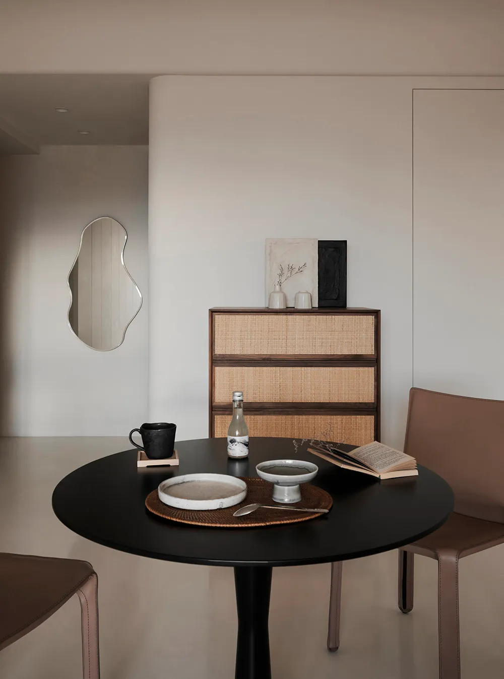 A minimalistic dining room featuring a black dining table with wooden accents and a decorative cabinet in the background.