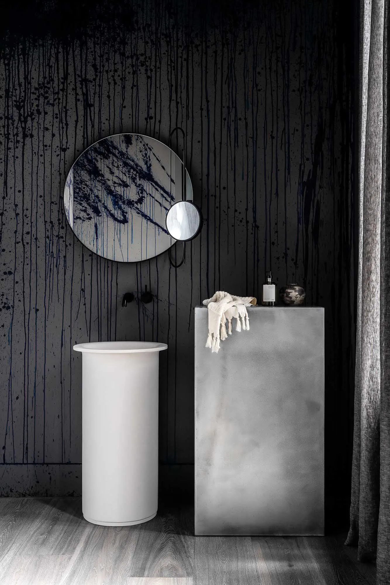 A modern bathroom featuring a minimalist design with concrete walls and a cylindrical pedestal sink.