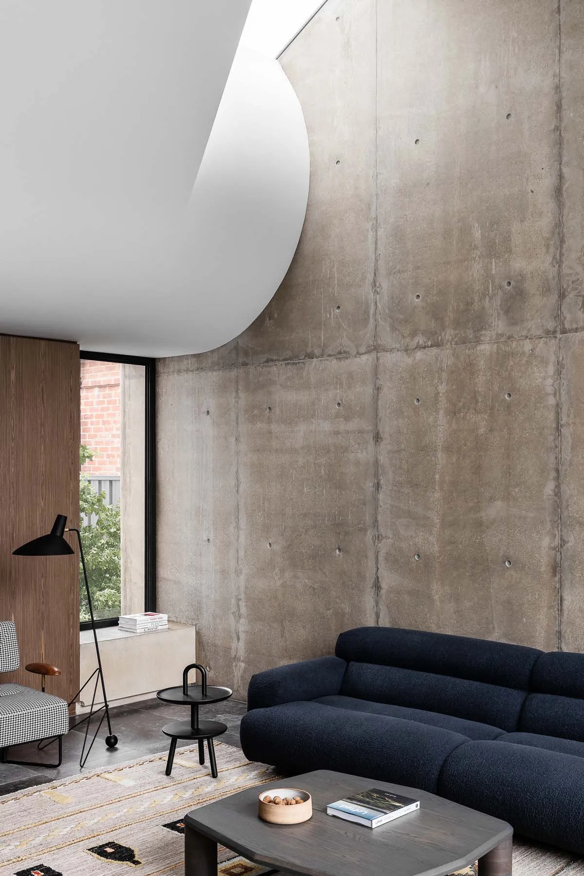 A minimalist living room featuring a concrete wall and floor, with a navy blue sofa and a dark wood coffee table.