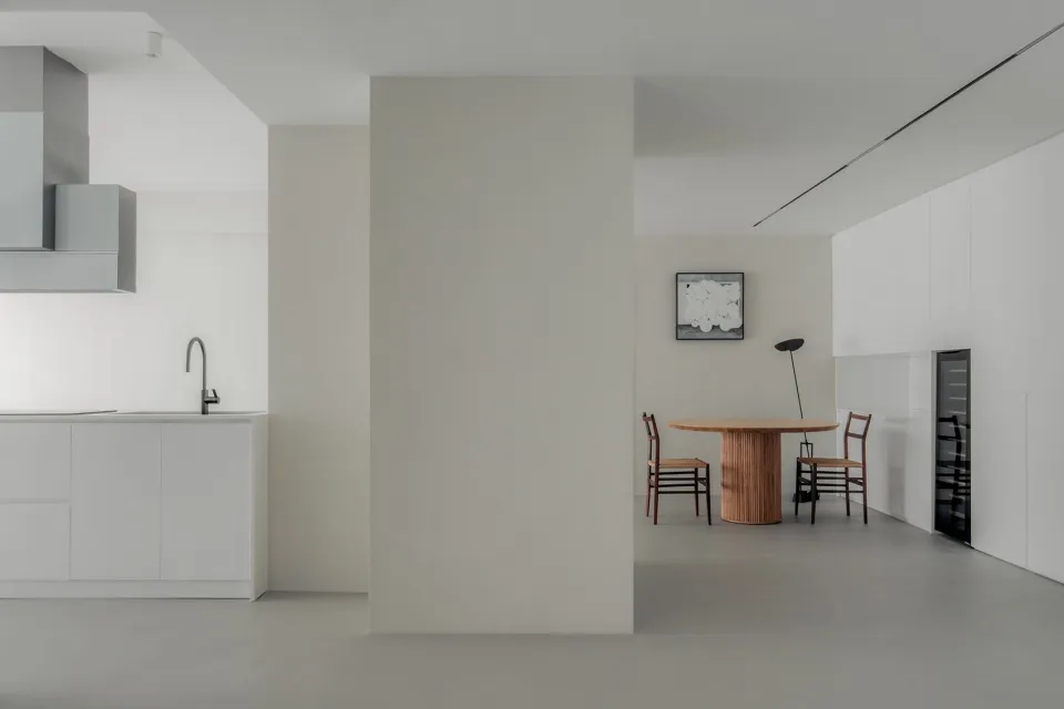 A minimalist kitchen with white cabinets and wooden flooring.