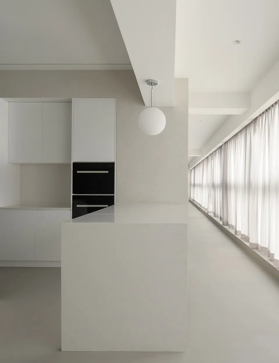 A minimalist residential kitchen with concrete countertops and white cabinets, featuring a cooking area and a long window wit
