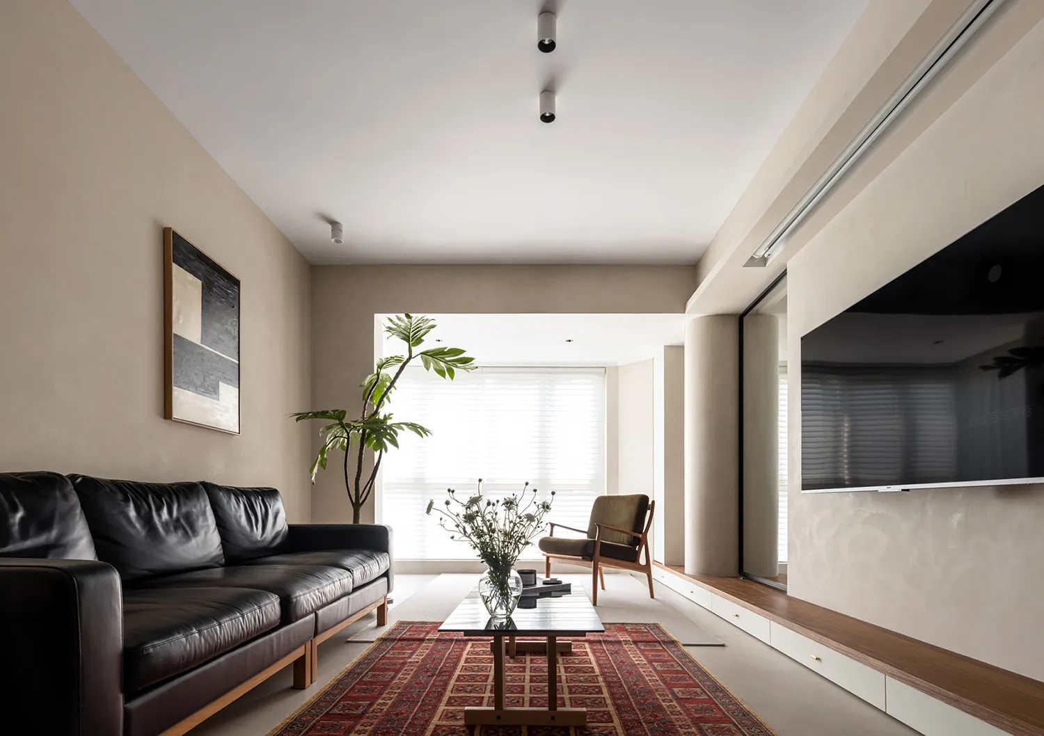 A modern residential living room with a black leather sofa, wooden armchair, and wooden coffee table on a red and brown patte