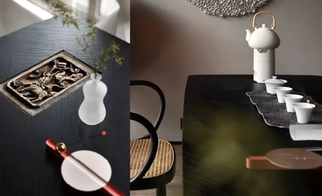 A sophisticated ceramic tea table setting with a white teapot and cups, a decorative plate, and a small vase with greenery.