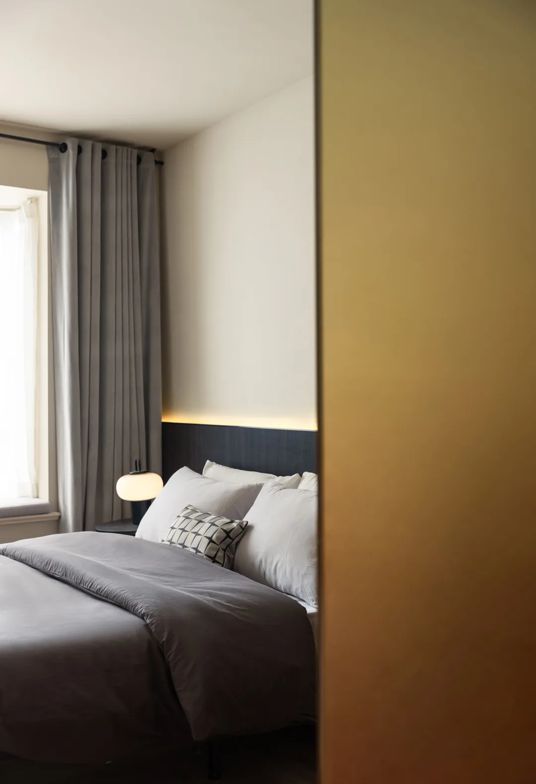 A minimalist bedroom with grey and white textiles and white pillows.