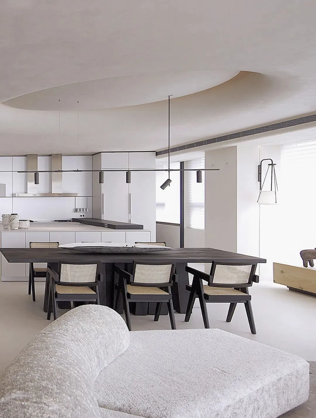 An image depicting a modern open-plan living, dining, and kitchen space featuring a concrete floor and a central wooden dinin