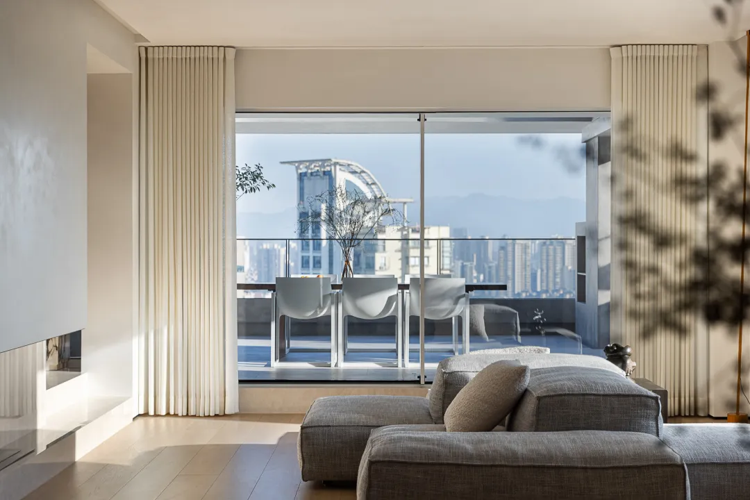 Modern living room with gray fabric seating, large windows, and cityscape view.