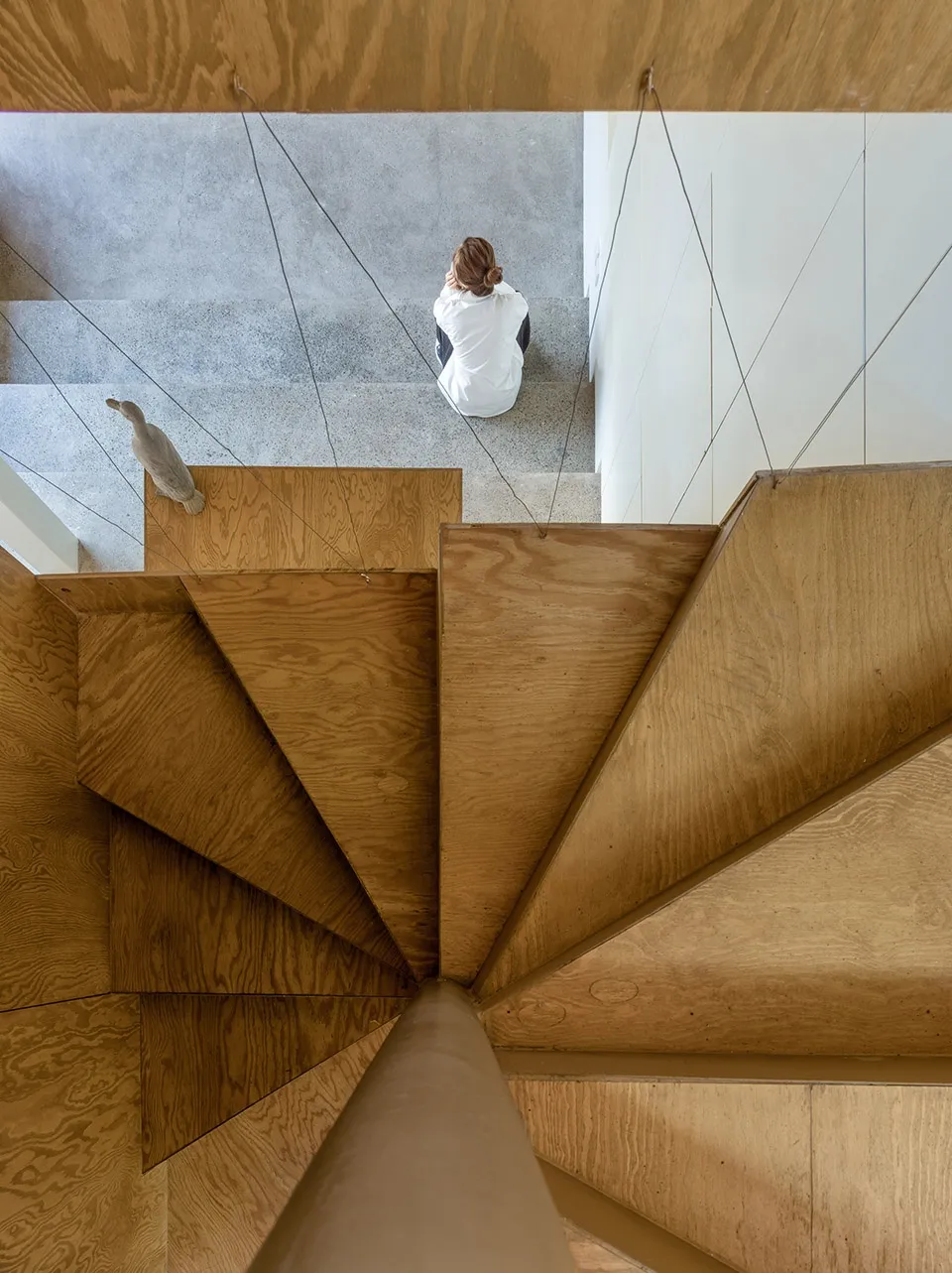 Modern wooden staircase with a person sitting on the steps and a bird sculpture.