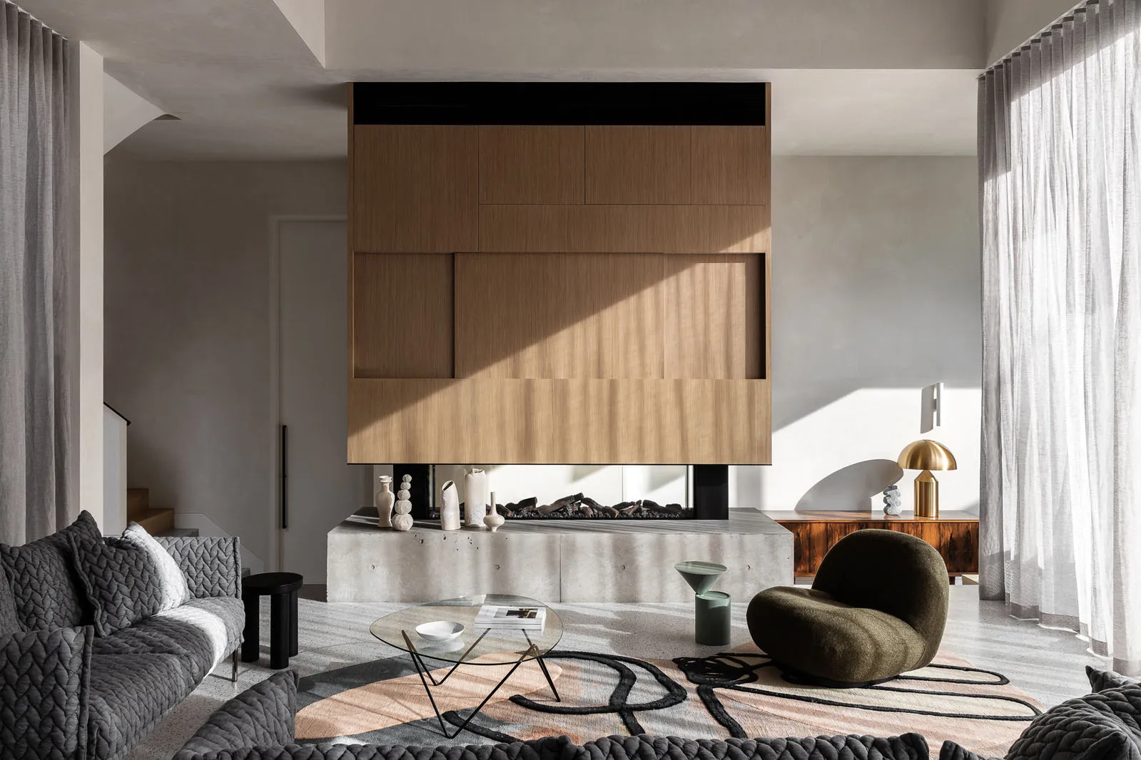 A modern living room featuring concrete walls and a fireplace, with a cozy armchair and a minimalist coffee table.