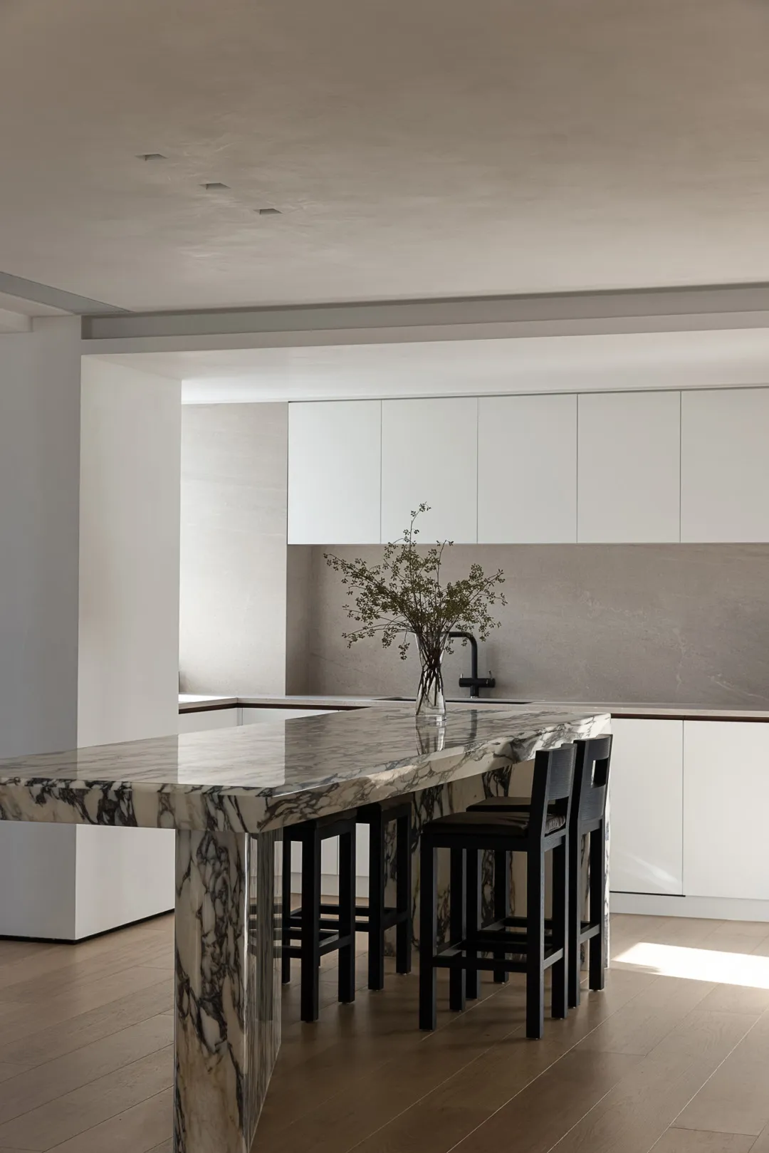 Modern minimalist kitchen with marble countertops and black stools.