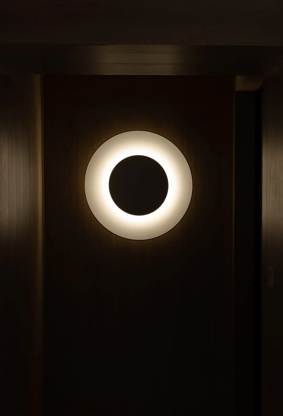 A minimalist wall light fixture with a white circular design and a metal finish.