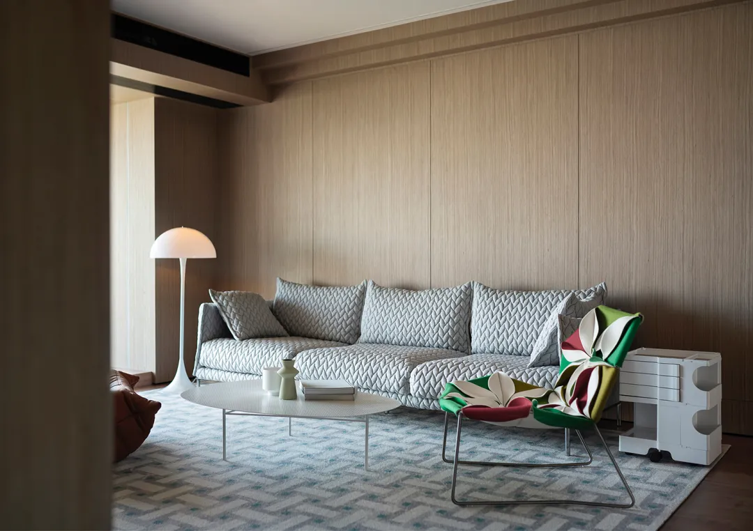 Modern living room with wooden paneled walls, grey sofa, and white coffee table.
