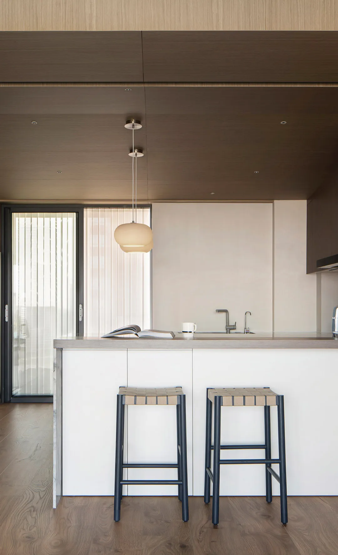 A modern kitchen with a wooden ceiling and floor, featuring a kitchen island with bar stools and a sink.