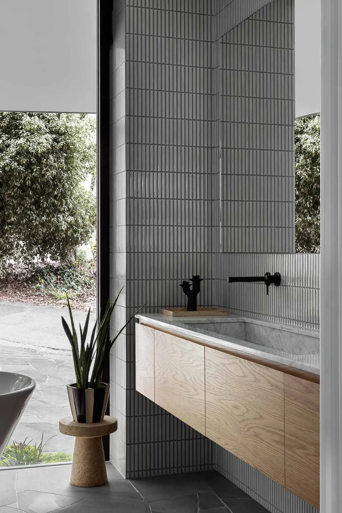 Modern bathroom with a geometric tiled wall, marble sink counter, and wooden cabinet.