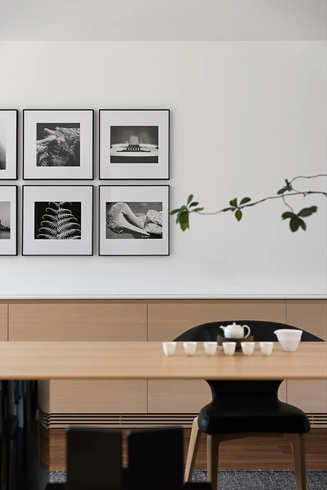 A minimalist dining room featuring wooden furniture with a modern black chair and a white tea set.