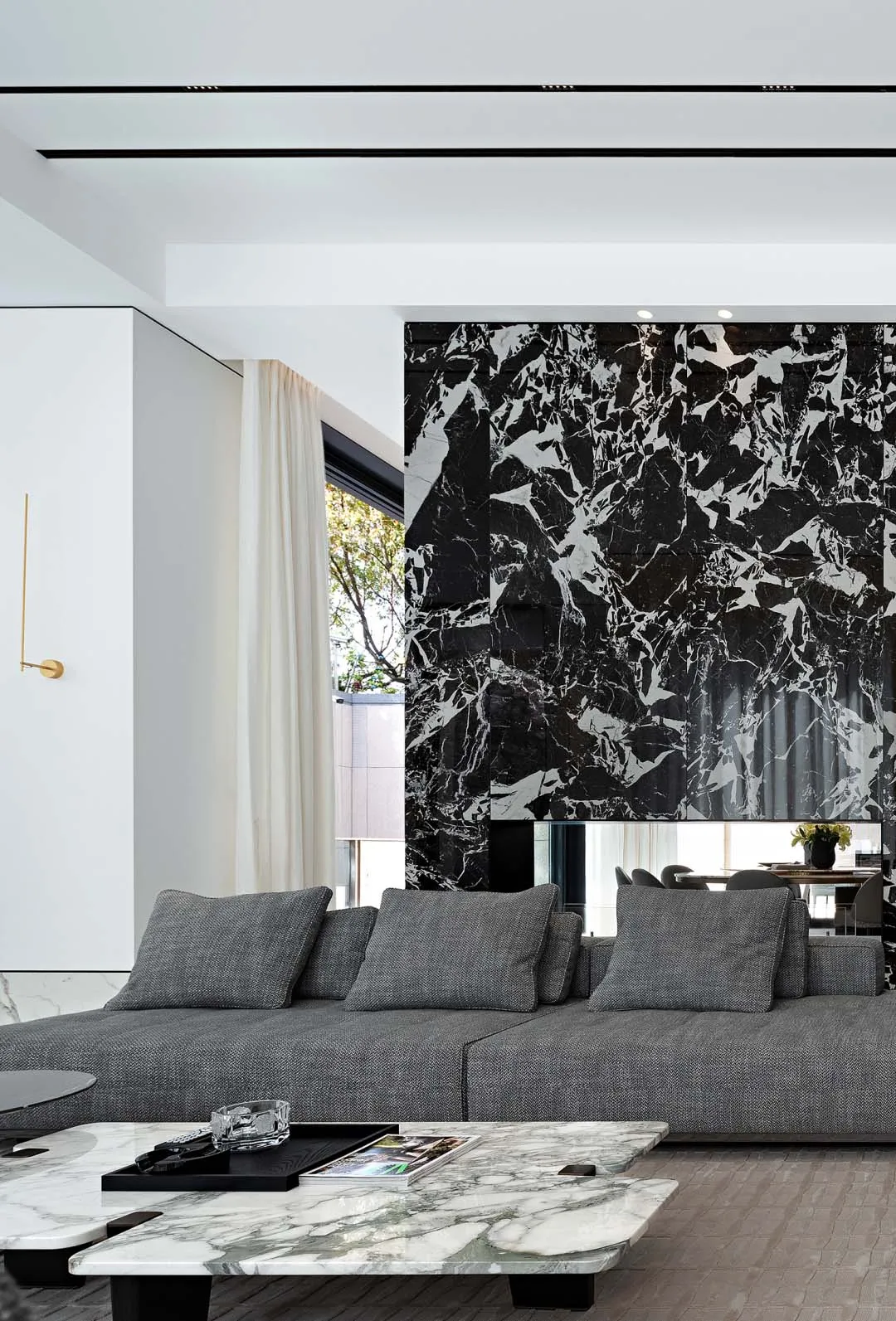 A modern living room with a white marble wall, a grey sofa, and a marble coffee table.