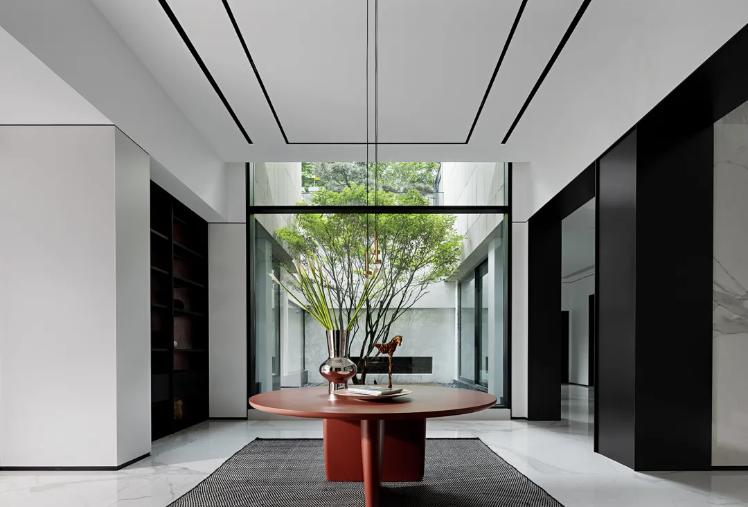 A minimalist living room with a metal table centerpiece, surrounded by white walls and black accents, featuring greenery outs