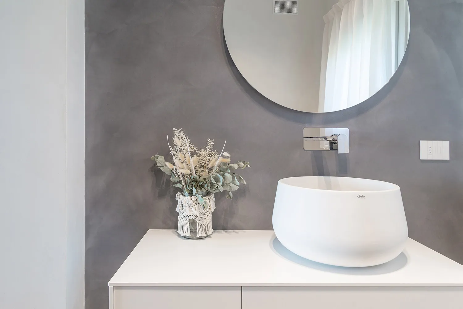 Modern minimalist bathroom with concrete walls and glass sink, featuring natural light and sparse decor.