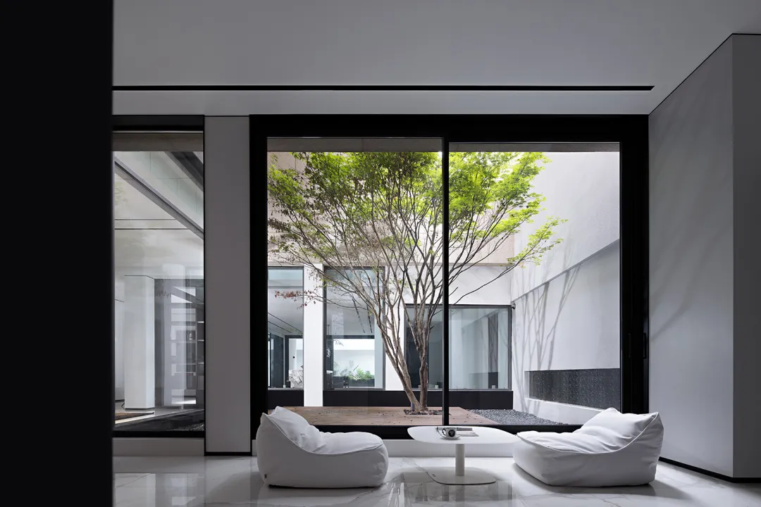 A minimalist modern living room with glass windows and white furniture.