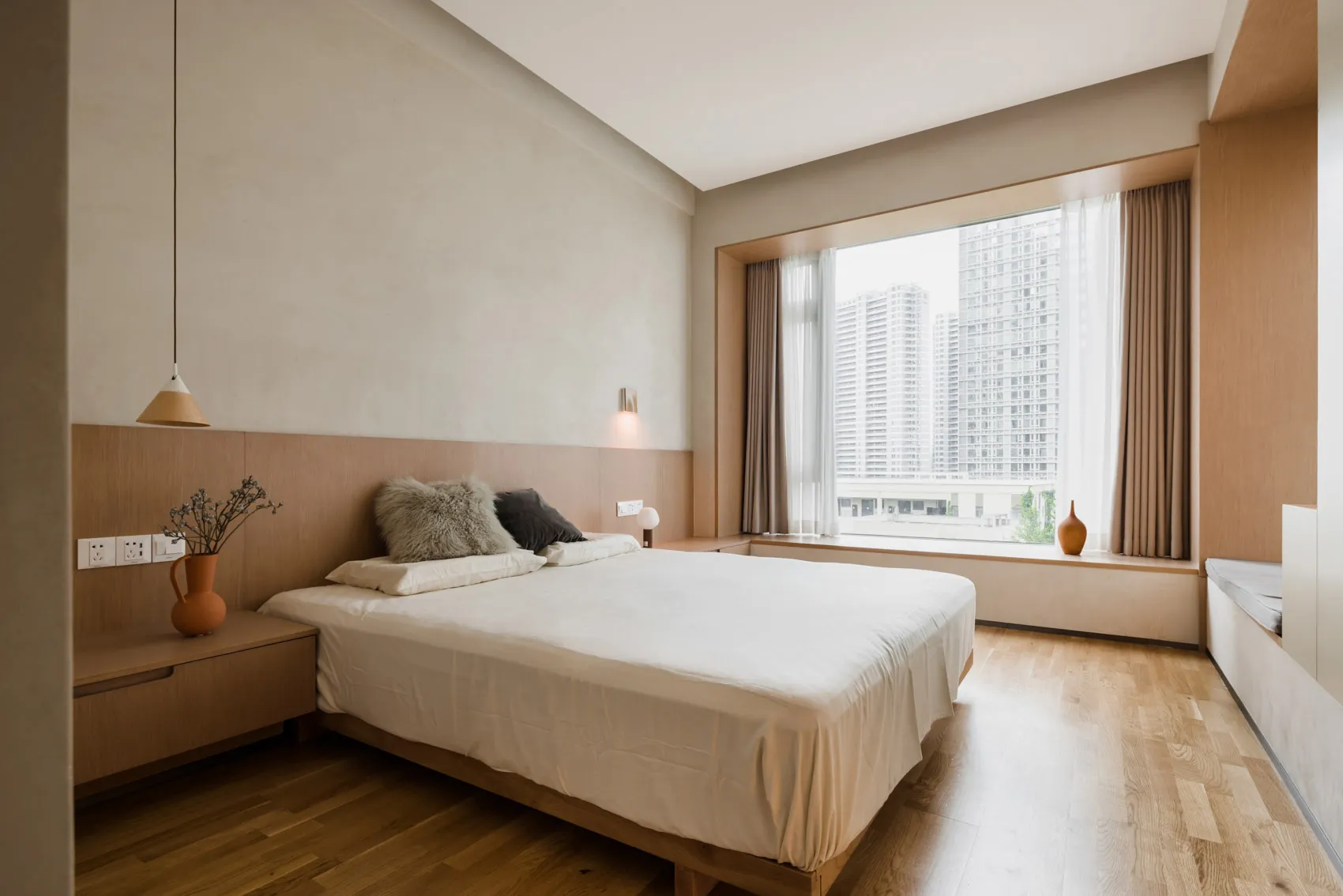 一間現代簡約臥室，搭配木質家具與大型窗戶，窗外可眺望城市景觀。