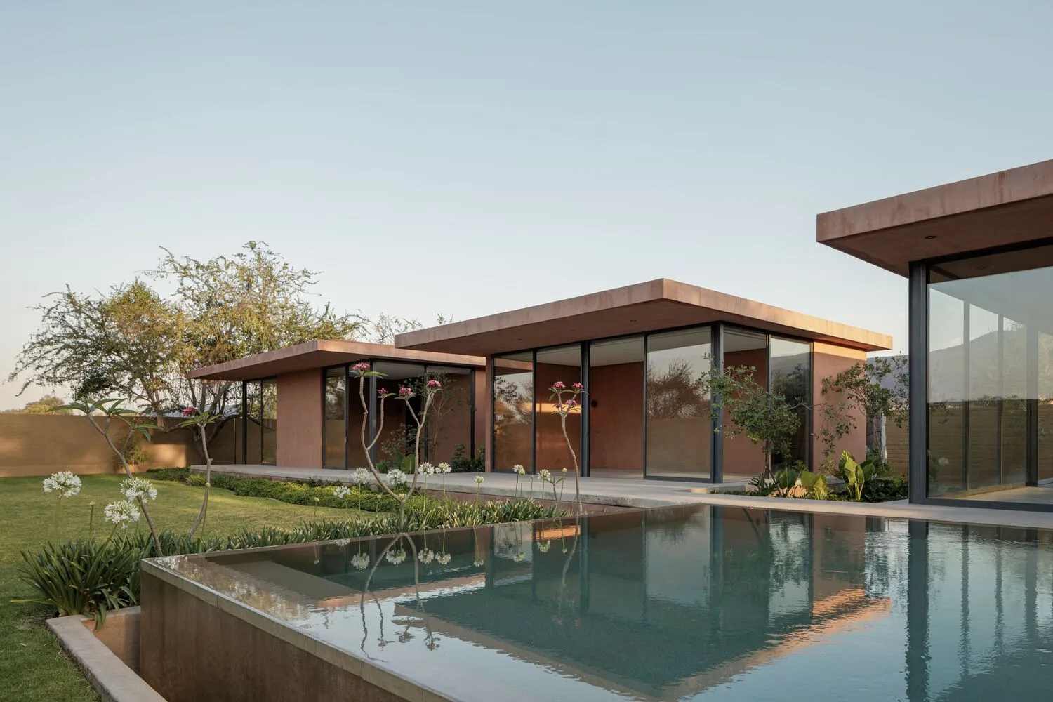 A modern residential house with a swimming pool made of concrete, surrounded by glass windows and metal structures.