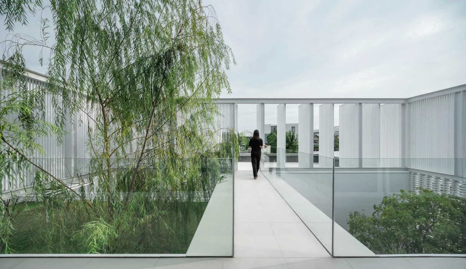 A modern rooftop patio with glass walls and a glass floor, featuring greenery and a person walking.
