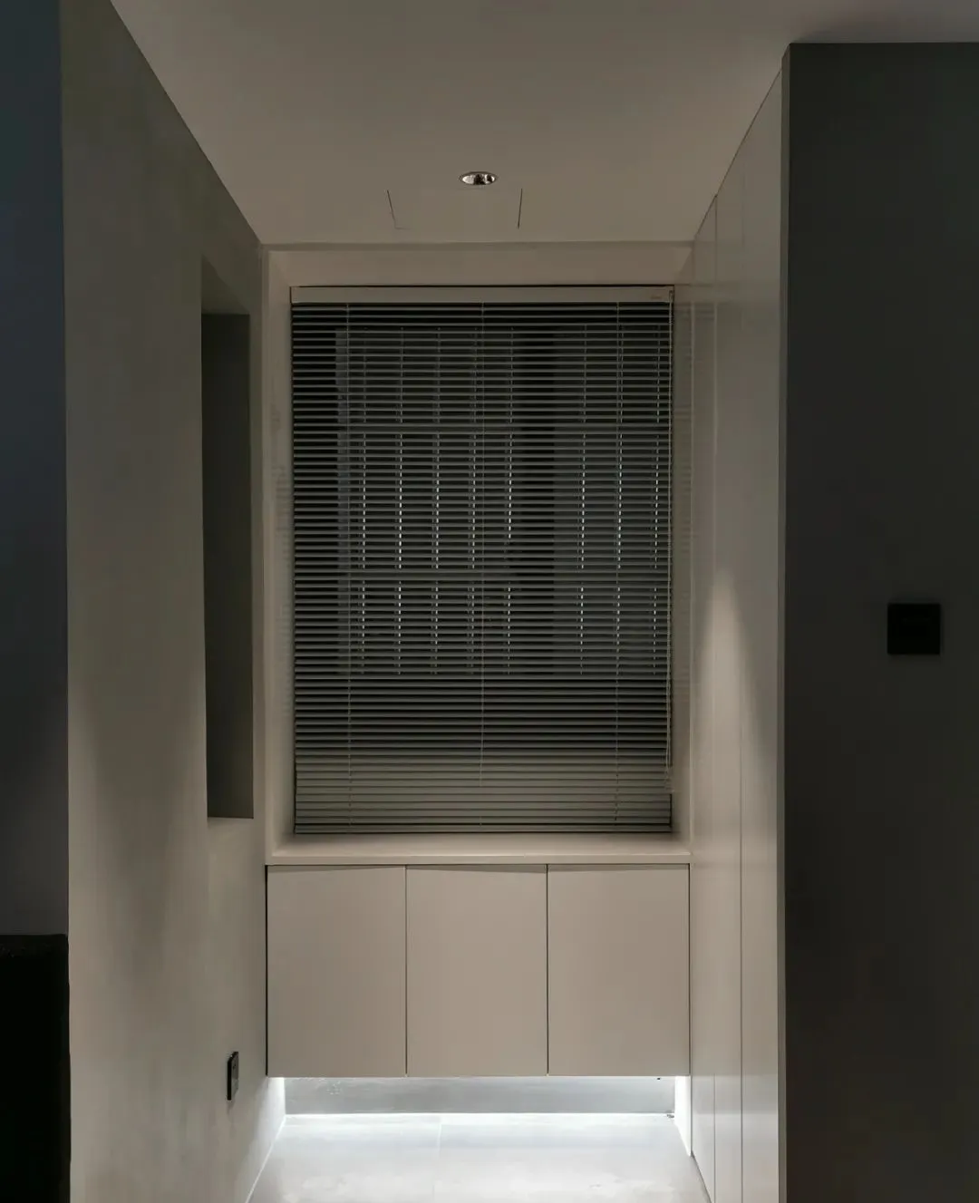 Modern, minimalist residential interior featuring metallic blinds and white cabinet storage.