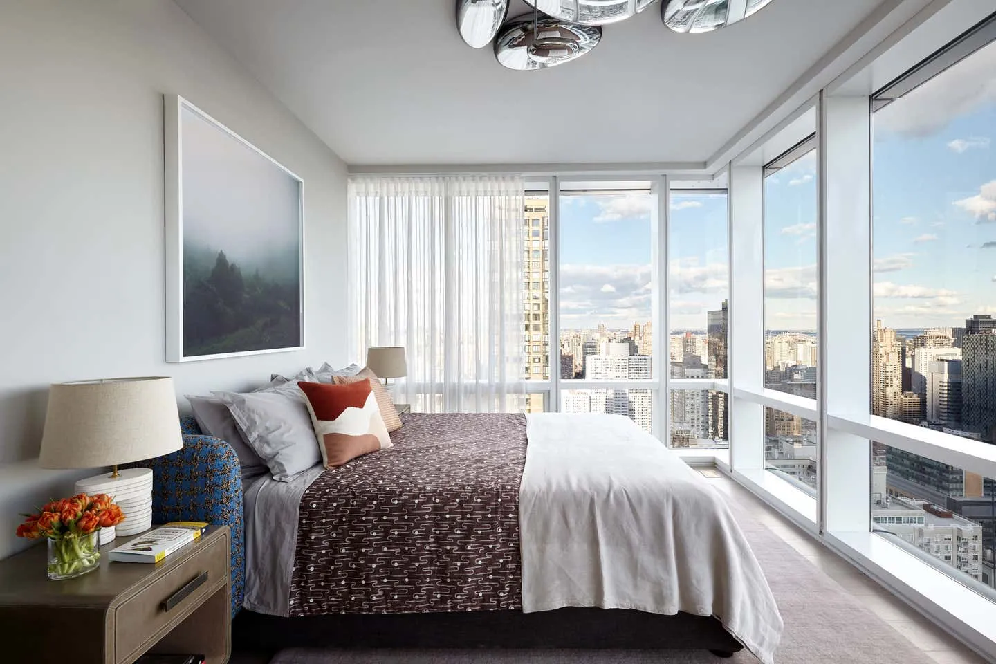 A modern bedroom featuring contemporary textiles, glass window frames, and a city view.