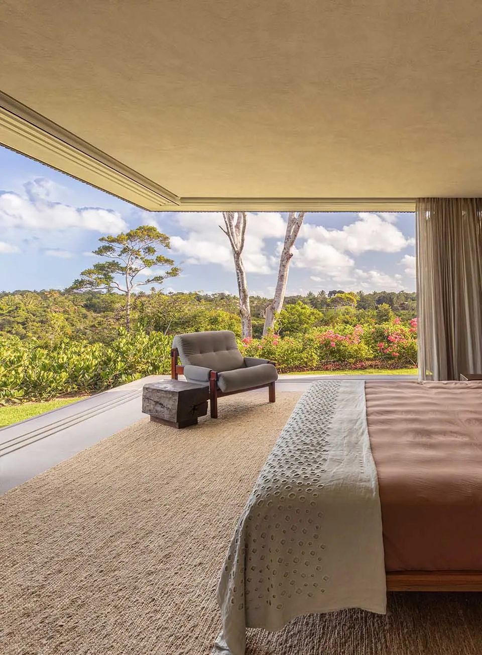 A minimalist bedroom featuring neutral colors and a view of lush greenery outside.